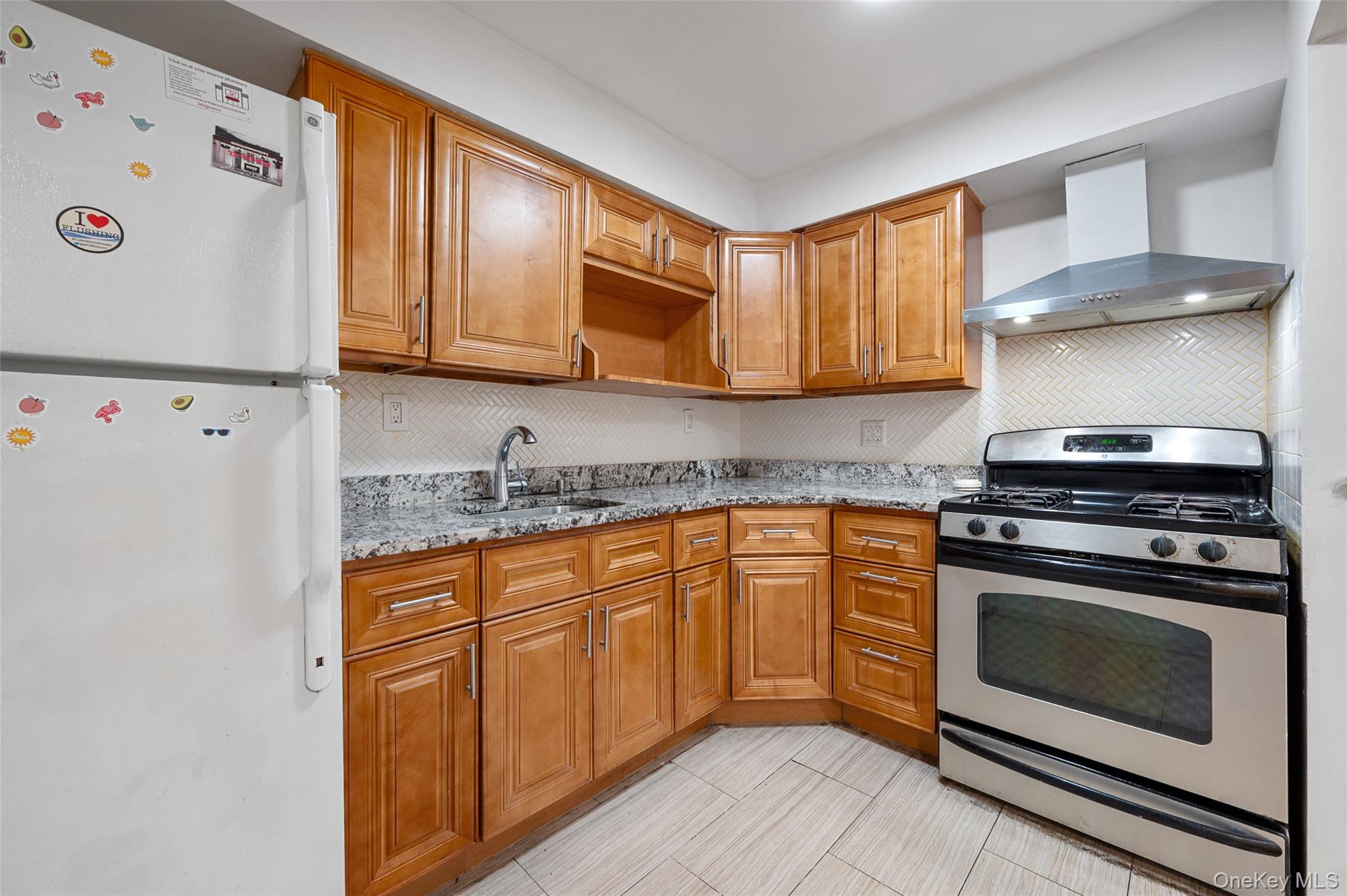 108-10 35th Avenue Queens, NY 11368 - Photo 6 of 29 Kitchen with freestanding refrigerator, stainless steel gas range oven, brown cabinets, wall chimney range hood, and light stone countertops