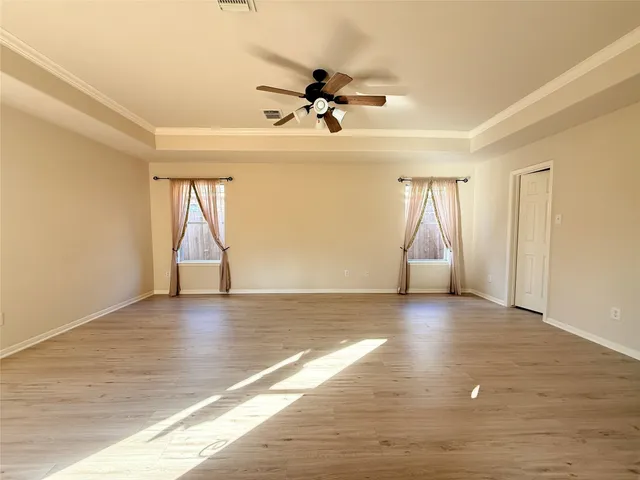 an empty room with wooden floor fan and windows