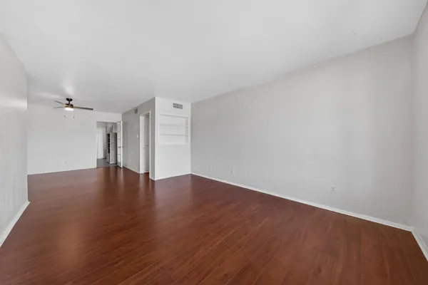 a view of an empty room with wooden floor and a ceiling fan