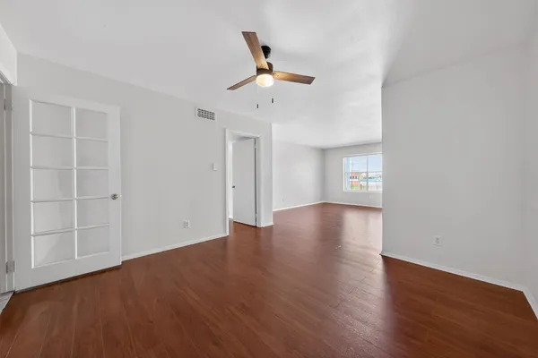 an empty room with wooden floor chandelier fan and windows