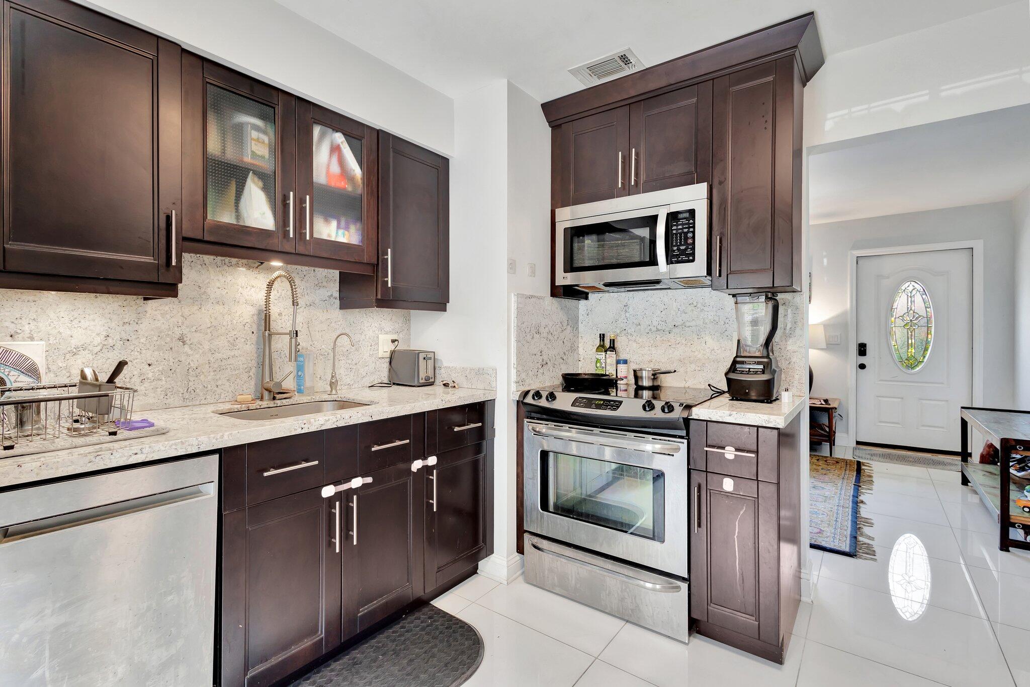 227 Northeast 12th Street, Unit 2 Delray Beach, FL 33444 - Photo 14 of 24 a kitchen with stainless steel appliances granite countertop a stove a sink dishwasher and a microwave oven with wooden cabinets