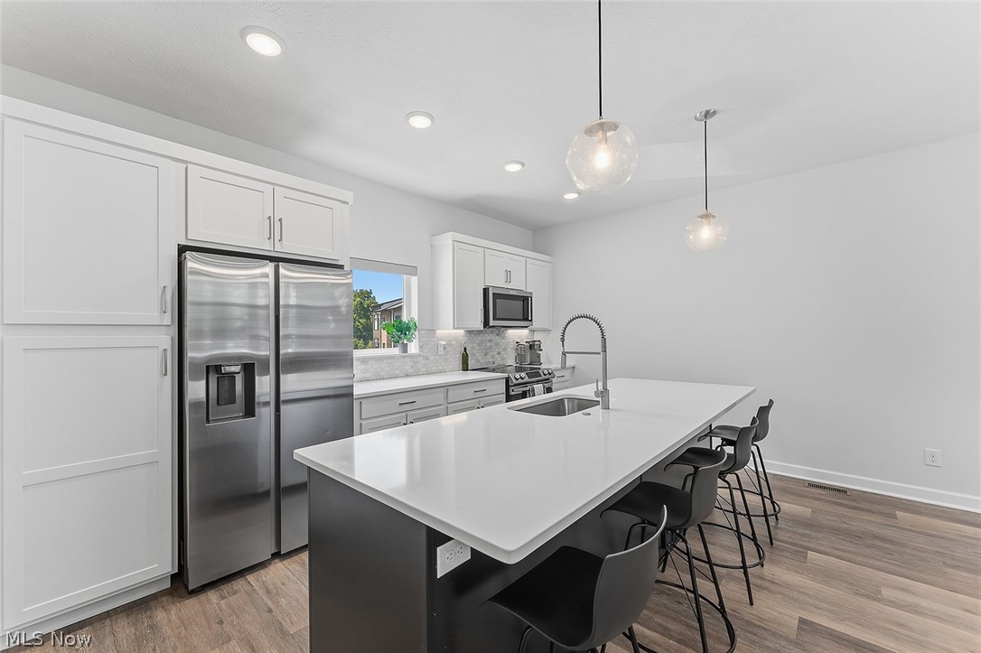 2308 Fulton Road Cleveland, OH 44113 - Photo 10 of 30 Kitchen featuring an island with seating, stainless steel appliances, white cabinetry, a tile backsplash, and recessed lighting