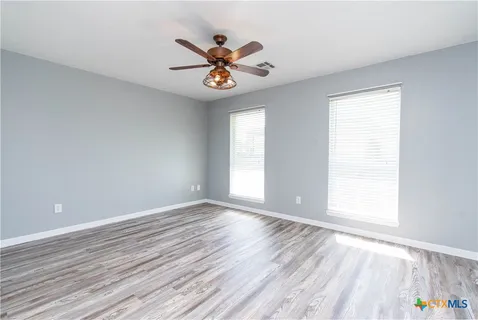 an empty room with wooden floor fan and windows