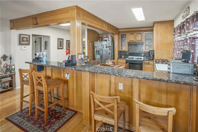 a kitchen with stainless steel appliances granite countertop a stove top oven a sink a dining table and chairs with wooden floor