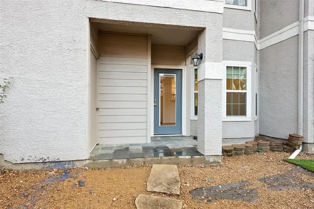 a view of a brick house with a yard plants and large tree