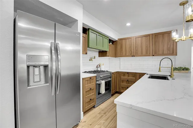 a kitchen with stainless steel appliances granite countertop a refrigerator a sink a stove and white cabinets with wooden floor