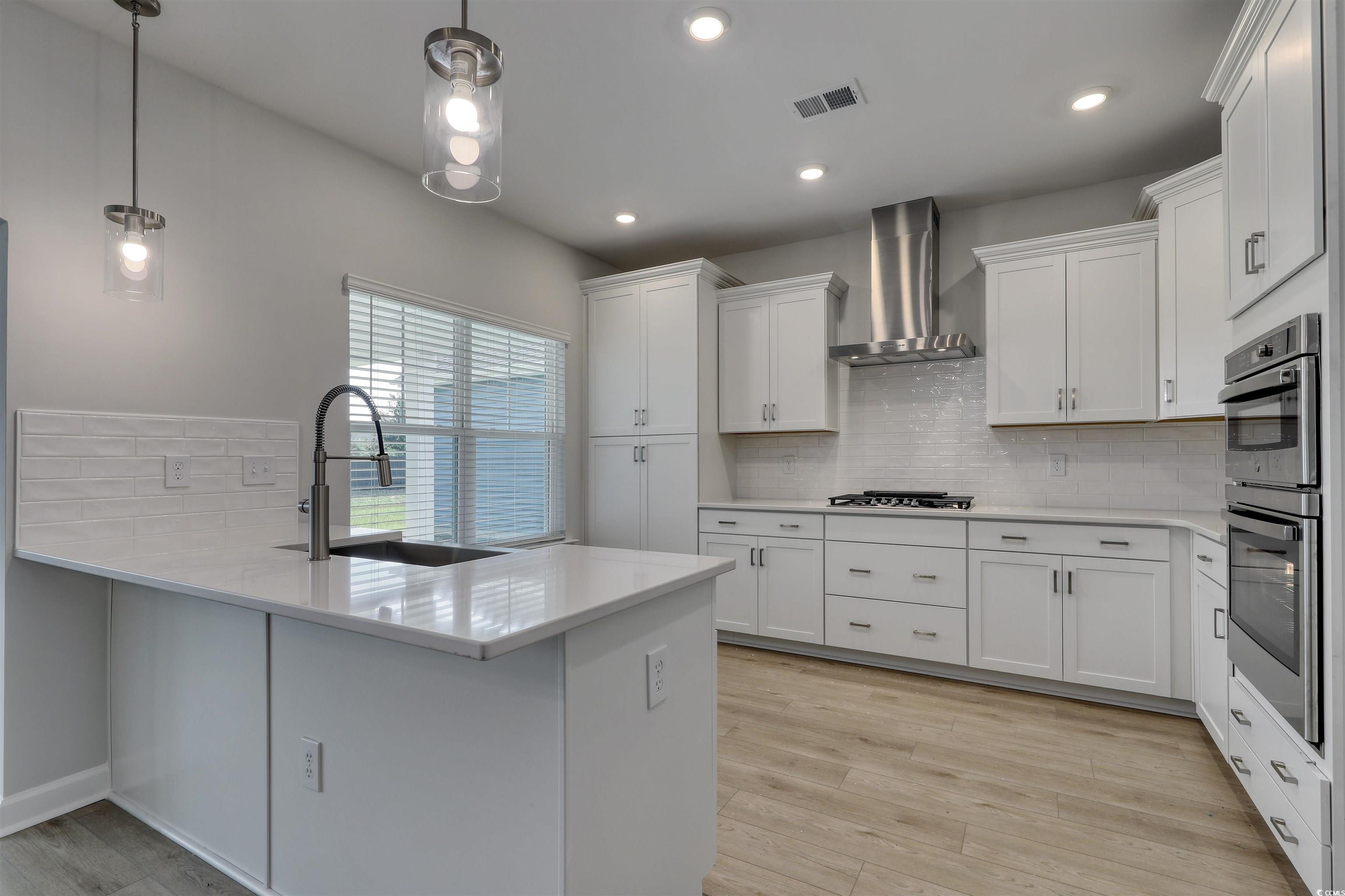 1083 Laconic Drive Myrtle Beach, SC 29588 - Photo 6 of 40 Kitchen featuring backsplash, decorative light fixtures, white cabinets, light stone countertops, and wall chimney range hood