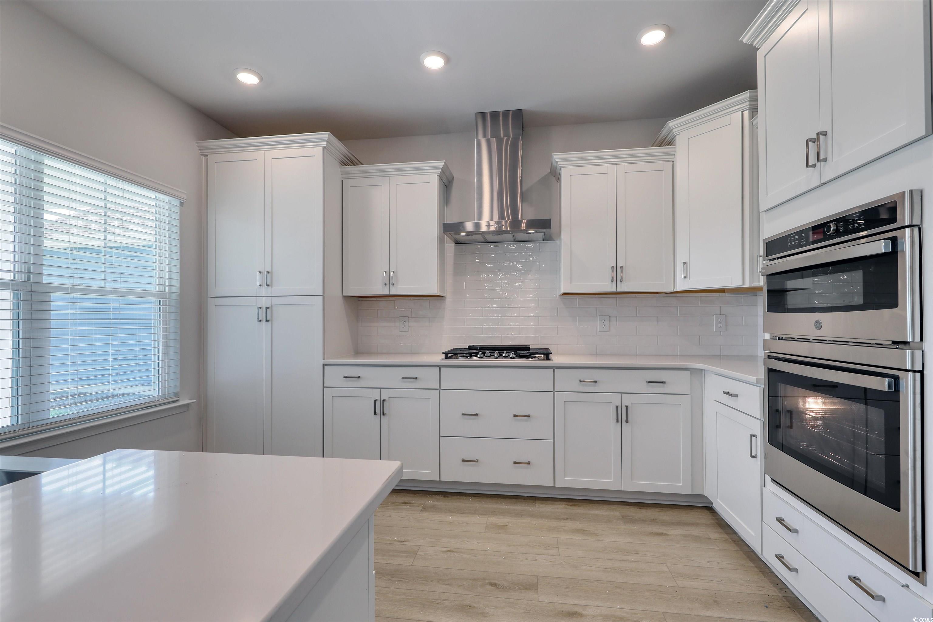 1083 Laconic Drive Myrtle Beach, SC 29588 - Photo 7 of 40 Kitchen with stainless steel appliances, wall chimney exhaust hood, decorative backsplash, white cabinetry, and recessed lighting