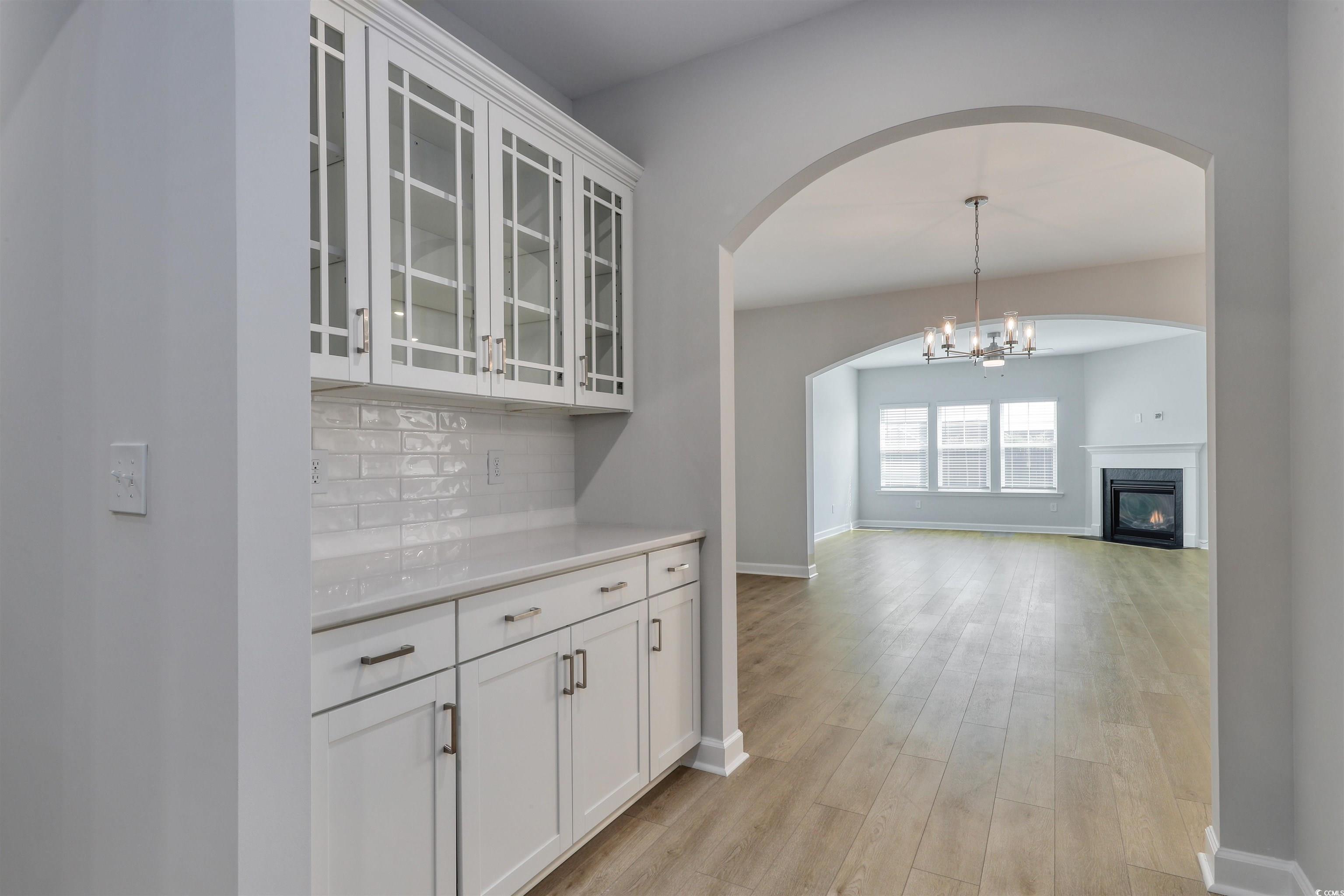 1083 Laconic Drive Myrtle Beach, SC 29588 - Photo 9 of 40 Bar featuring glass insert cabinets, white cabinets, arched walkways, tasteful backsplash, and light wood-style flooring