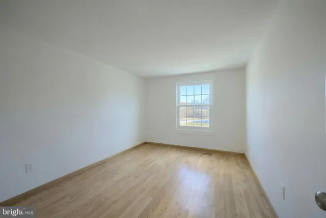 a view of an empty room with wooden floor and window