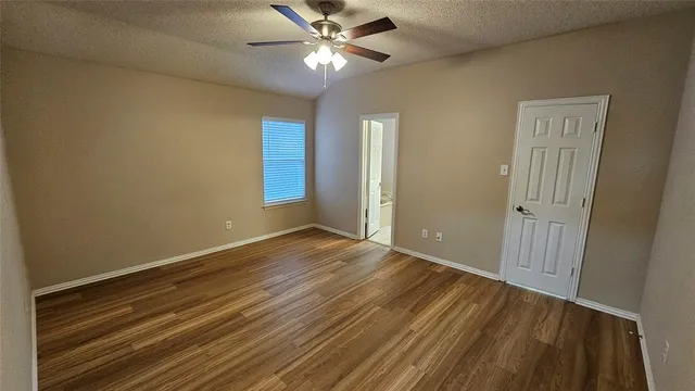 a view of an empty room with wooden floor and a ceiling fan