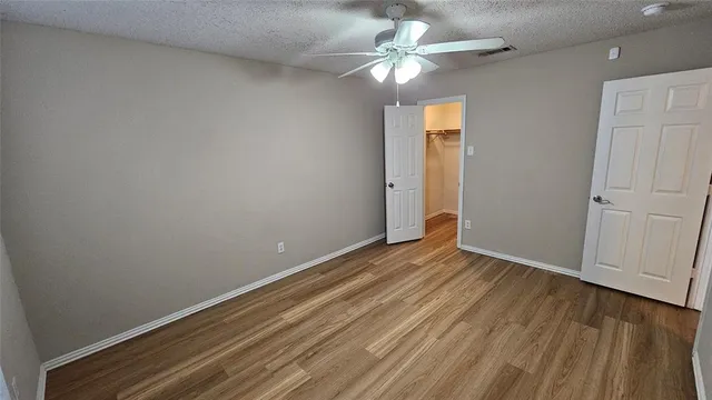 an empty room with wooden floor fan and windows
