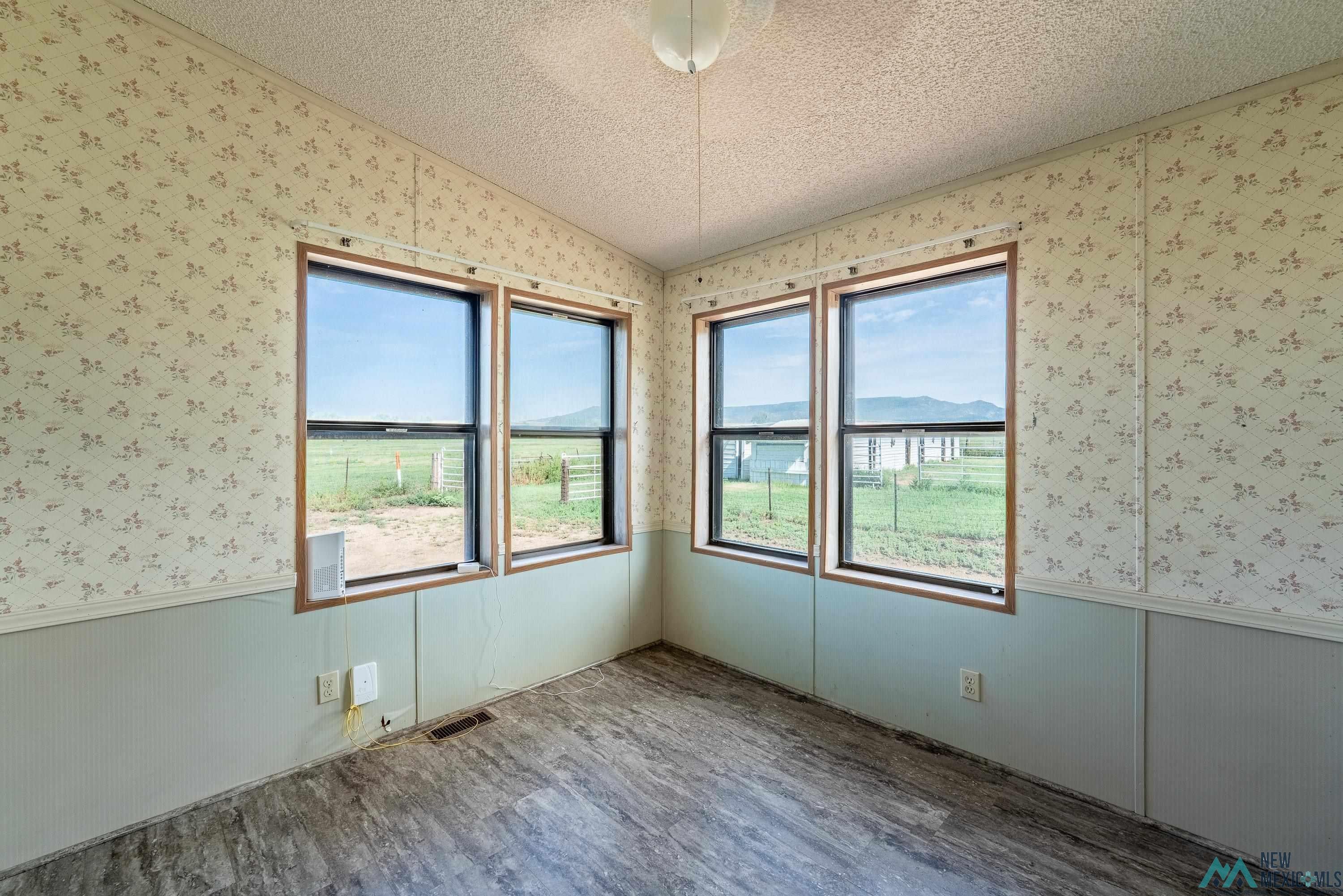 35234 Highway 87 Raton, NM 87740 - Photo 42 of 90 Empty room featuring a textured ceiling, wood finished floors, wallpapered walls, wainscoting, and vaulted ceiling