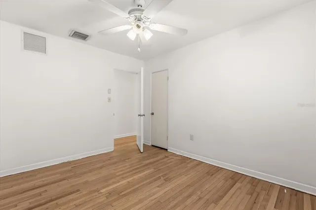 an empty room with wooden floor and fan