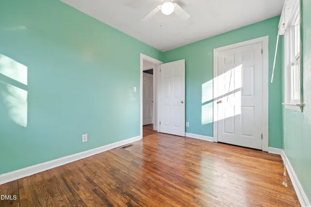 a view of empty room with wooden floor and fan