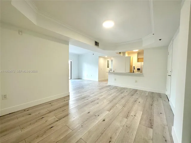 an empty room with wooden floor and a kitchen