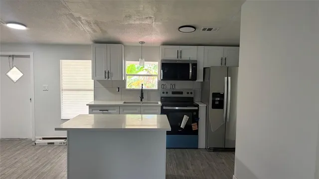 a kitchen with kitchen island a counter top space appliances a sink and a window