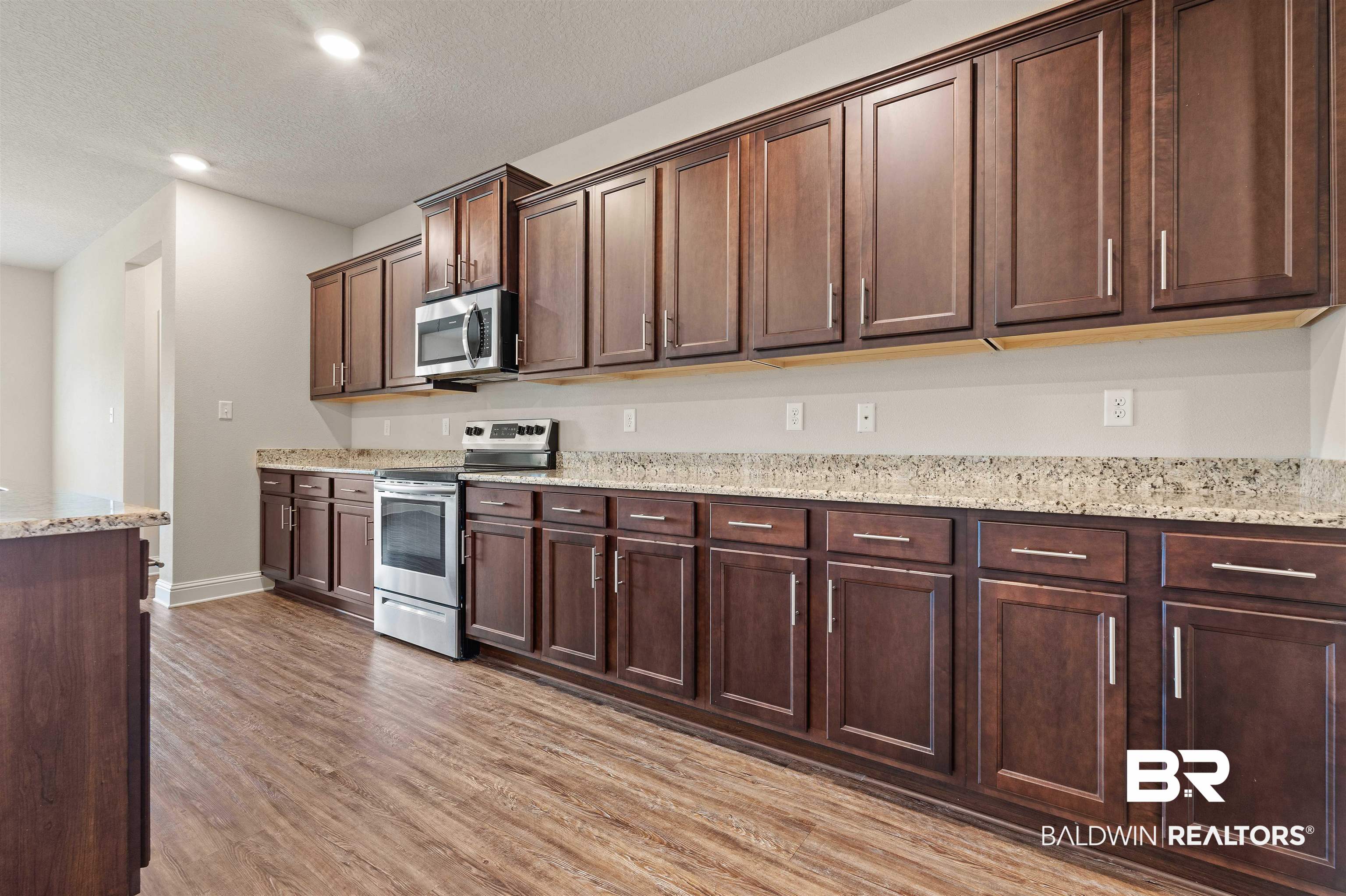 1864 Gwin Court Mobile, AL 36695 - Photo 10 of 37 Kitchen featuring appliances with stainless steel finishes, dark brown cabinets, light stone counters, light hardwood / wood-style floors, and a textured ceiling