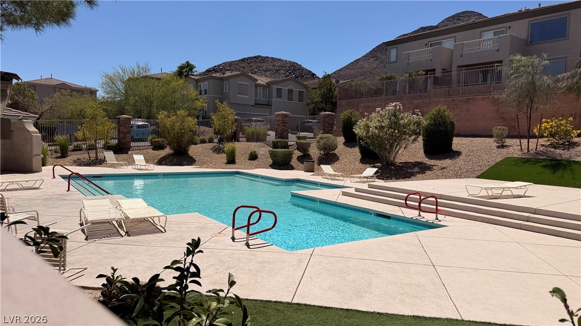754 Solitude Point Avenue Henderson, NV 89012 - Photo 2 of 38 A refreshing outdoor pool with comfortable lounge seating, set against a backdrop of modern homes and desert hills.