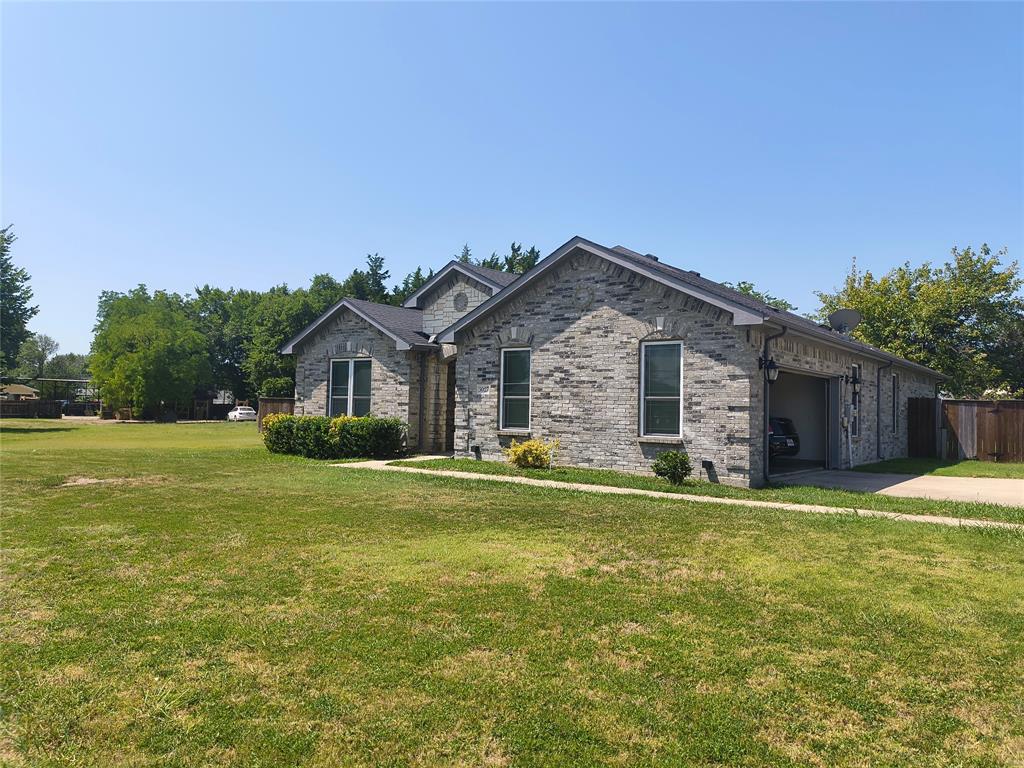 Grey brick exterior with multiple window openings, an attached garage, a dark asphalt shingle roof, a concrete driveway, and front landscaping