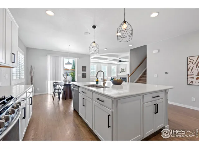 a kitchen with kitchen island granite countertop a sink appliances wooden floor and a view of living room