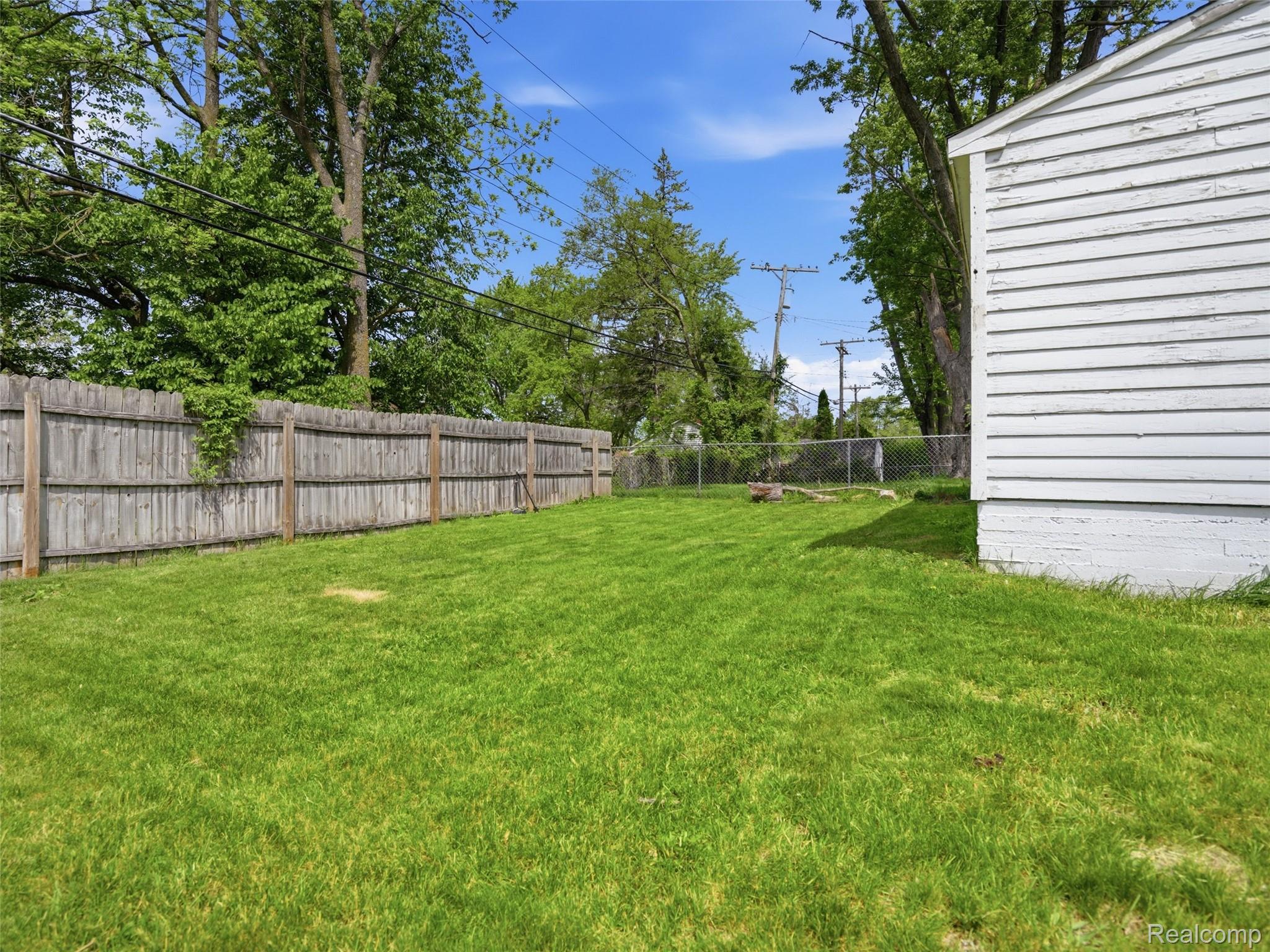 320 South Avery Road Waterford, MI 48328 - Photo 6 of 25 Expansive lawn area featuring wood privacy fencing, mature trees, and a white-sided exterior structure