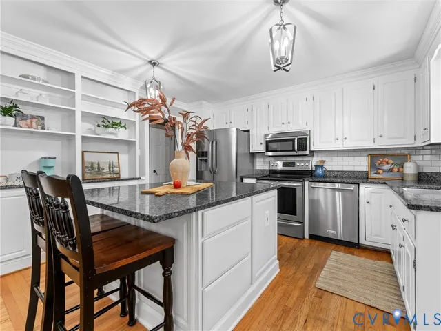 a kitchen with stainless steel appliances granite countertop a stove a refrigerator a sink dishwasher a dining table and chairs with wooden floor