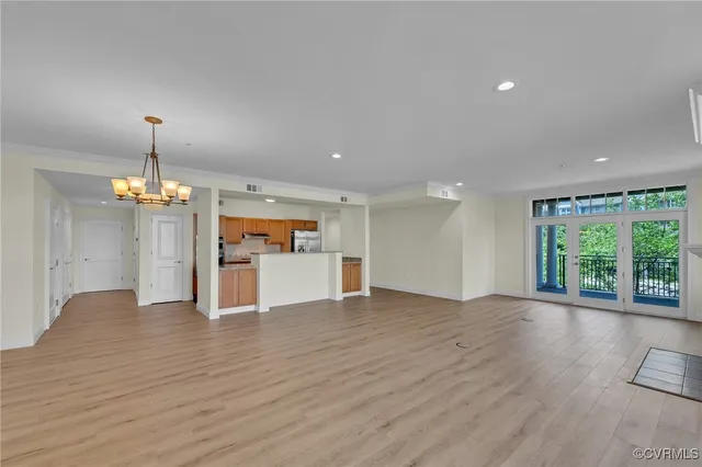 a view of an empty room with wooden floor kitchen view and a window