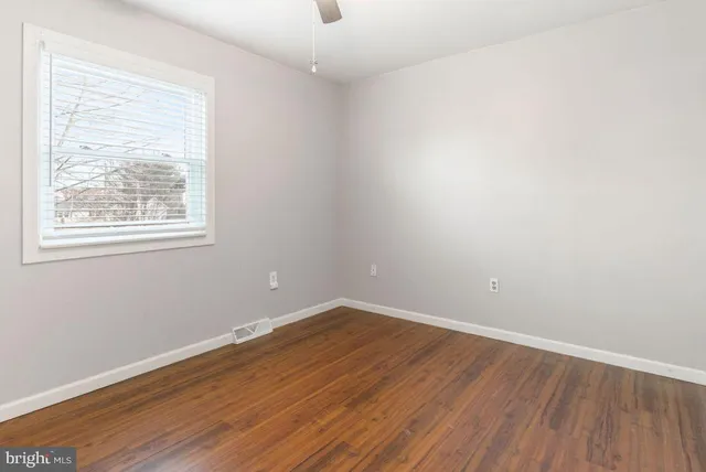 an empty room with wooden floor chandelier fan and windows