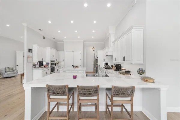 a large kitchen with stainless steel appliances kitchen island granite countertop a stove a sink a refrigerator and a white cabinets with wooden floor