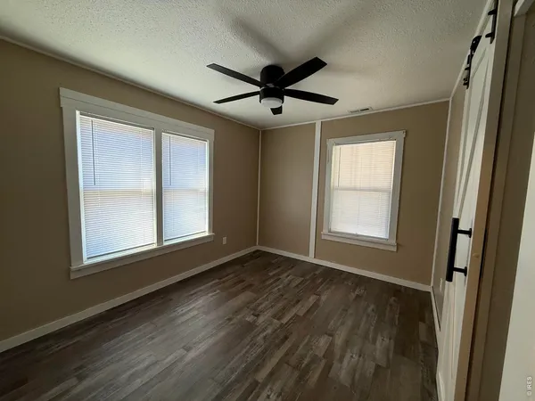 an empty room with wooden floor a ceiling fan and windows