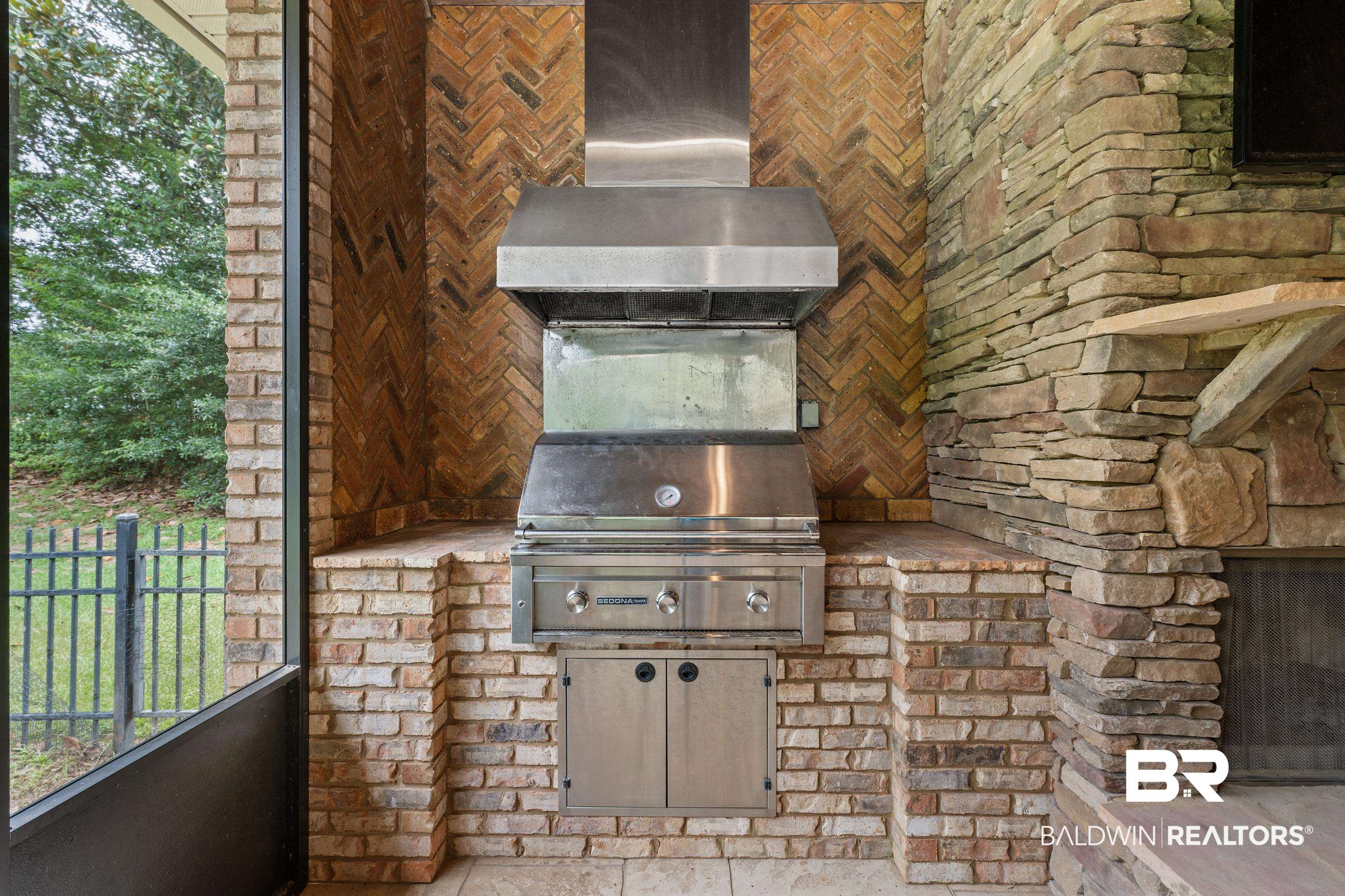 30463 Dolive Ridge Daphne, AL 36527 - Photo 22 of 58 Outdoor kitchen featuring a built-in stainless steel grill with a matching hood, brick masonry in a herringbone pattern, natural stone wall accents, and an integrated appliance cabinet