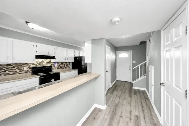 a kitchen with stainless steel appliances a microwave a stove a sink dishwasher a refrigerator and white cabinets with wooden floor