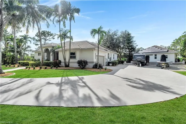 a view of a white house with a yard plants and palm trees