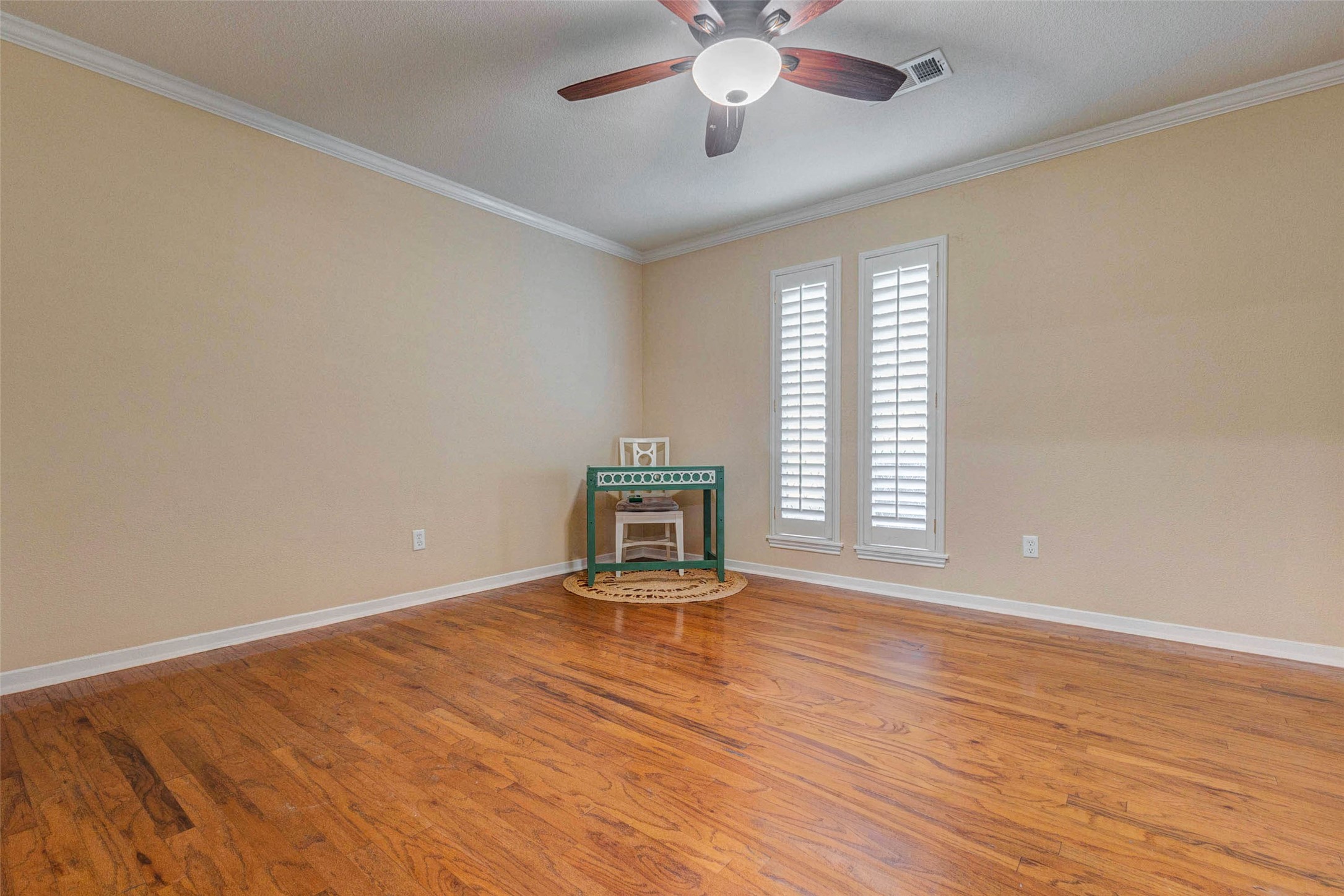 6710 Falling Waters Drive Spring, TX 77379 - Photo 25 of 46 The flex room features warm hardwood flooring, neutral walls, and a ceiling fan. It is well-lit with natural light from two tall windows with shutters, creating a cozy and inviting atmosphere.