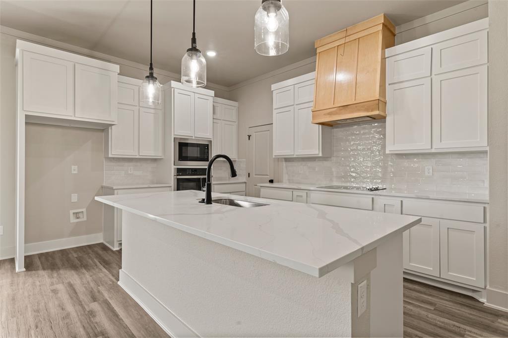 138 Dana Pt Road Lorena, TX 76655 - Photo 8 of 24 Kitchen featuring a central island with an undermount sink, white cabinetry, a built-in microwave, wood-finish flooring, and a decorative wood range hood