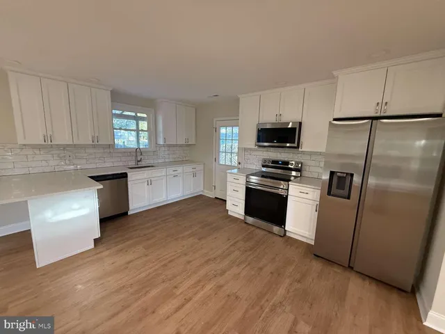 a kitchen with granite countertop a refrigerator oven a sink a stove and white cabinets