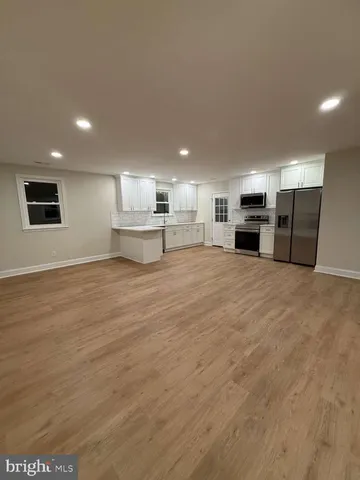 a large white kitchen with kitchen island a stove a sink a refrigerator with white cabinets and wooden floor