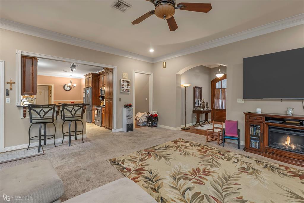 12168 Highway 157 Princeton, LA 71067 - Photo 16 of 32 Living area with light carpet, a ceiling fan, crown molding, a lit fireplace, and arched walkways