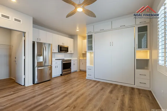 a view of a kitchen with a refrigerator a ceiling fan wooden floor and a kitchen space