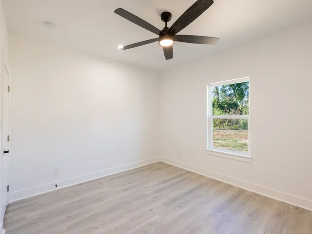 an empty room with wooden floor ceiling fan and windows
