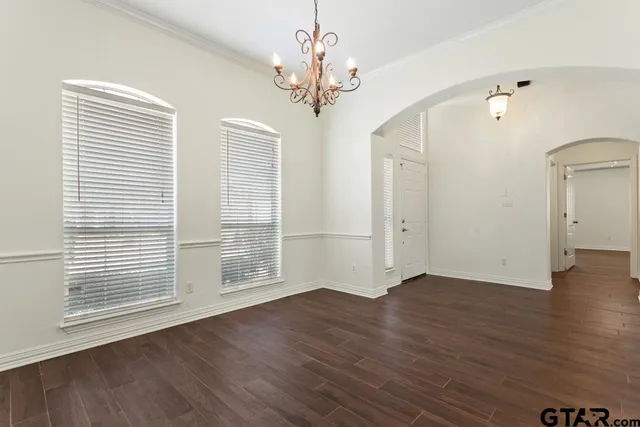 an empty room with wooden floor chandelier and windows
