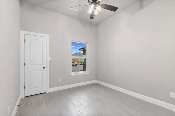 an empty room with wooden floor chandelier fan and windows