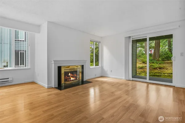 a view of an empty room with wooden floor fireplace and a window
