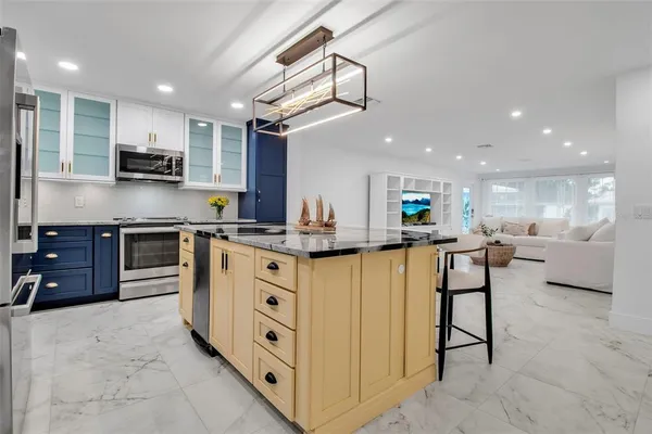 a kitchen with stainless steel appliances kitchen island granite countertop a stove top oven a sink a refrigerator and white cabinets