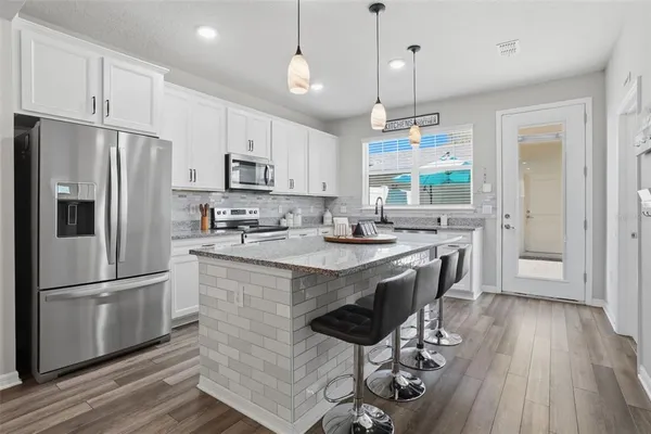 a kitchen with kitchen island granite countertop a refrigerator a stove a sink dishwasher a dining table and chairs with wooden floor