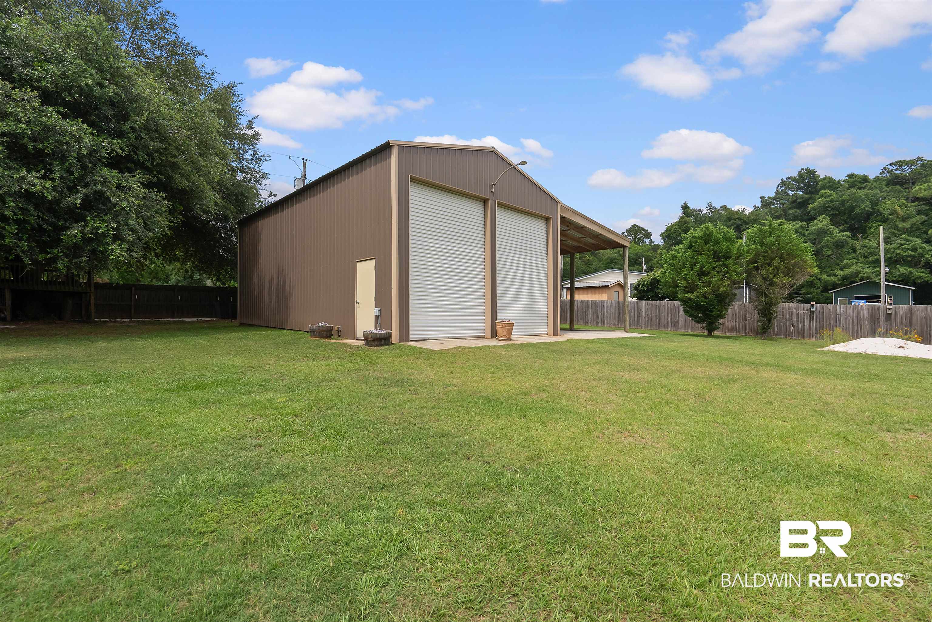 12070 Comalander Road Fairhope, AL 36532 - Photo 45 of 50 Metal outbuilding featuring two roll-up doors, an additional entry door, and an attached covered concrete pad