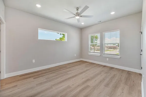 an empty room with wooden floor a ceiling fan and kitchen view