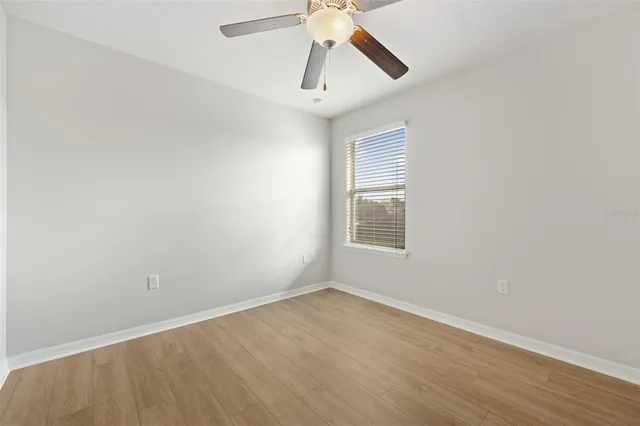 an empty room with wooden floor ceiling fan and windows