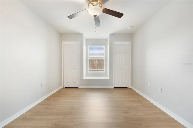 an empty room with wooden floor chandelier fan and windows
